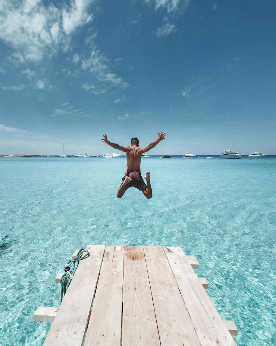 Homme en short de bain qui saute dans la mer turquoise depuis un ponton près d'une villa de luxe Le Collectionist à Ibiza