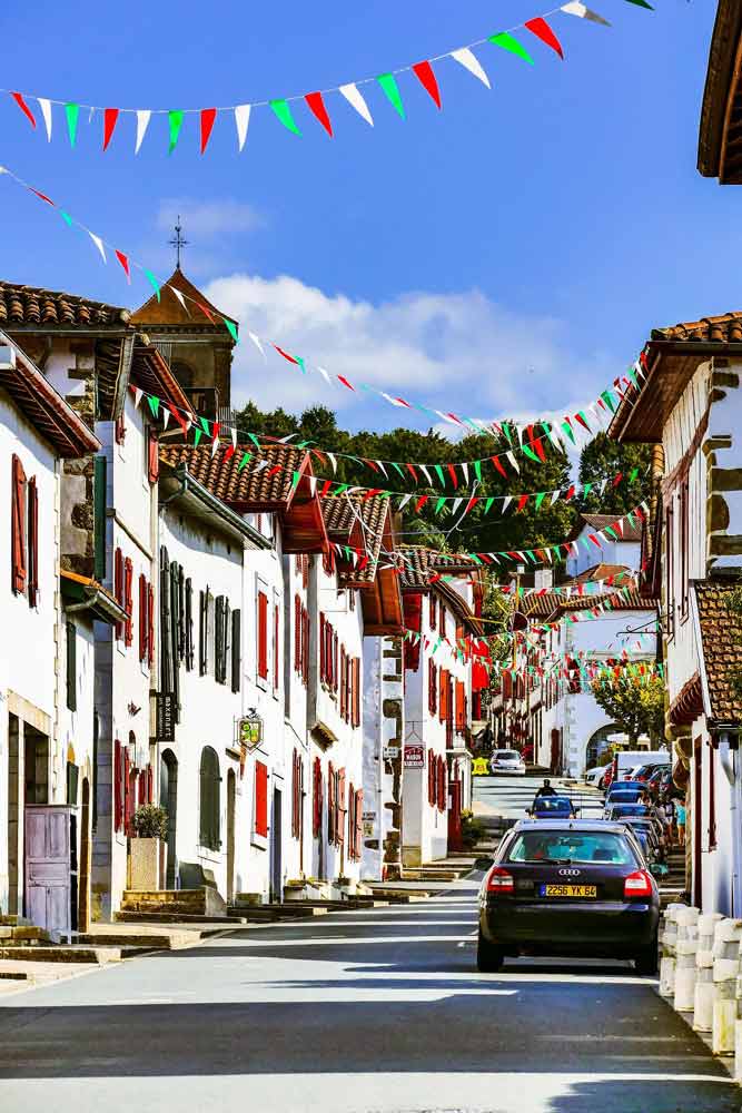 Rue de village au Pays basque décorée de fanions rouge, vert et blanc lors d’une fête locale, ambiance populaire mise en avant par Merkatu blog basque