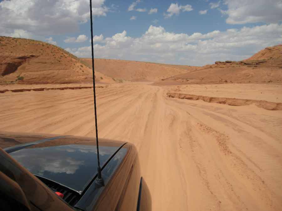 Piste de sable menant à Upper Antelope Canyon, paysage désertique de l’Arizona vu depuis un véhicule tout-terrain sous un ciel partiellement nuageux