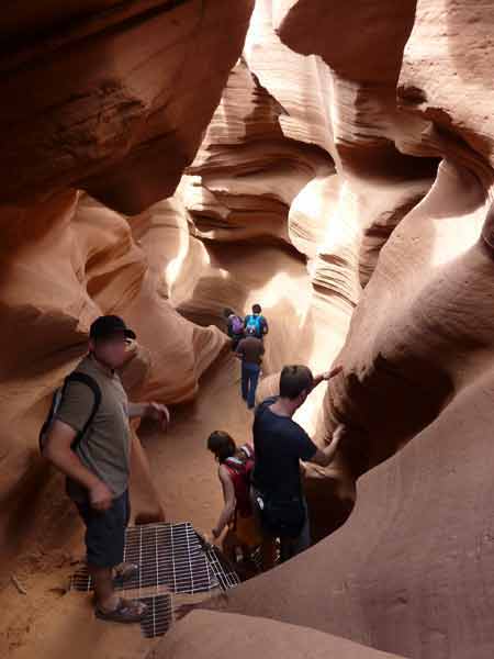Descente par échelle métallique dans le Lower Antelope Canyon, visiteurs évoluant entre des parois étroites sculptées par l’eau