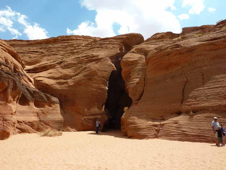 Entrée d’Upper Antelope Canyon creusée dans la roche de grès, parois sculptées par l’érosion et sol sablonneux sous la lumière du désert