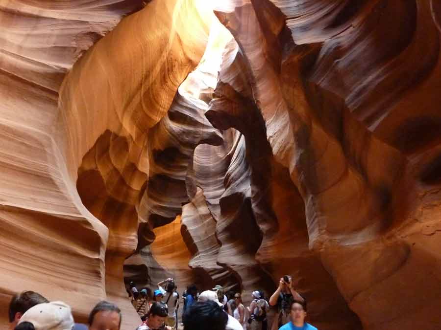 Intérieur d’Upper Antelope Canyon avec ses parois ondulées de grès illuminées par la lumière naturelle, visiteurs observant les jeux d’ombres et de couleurs