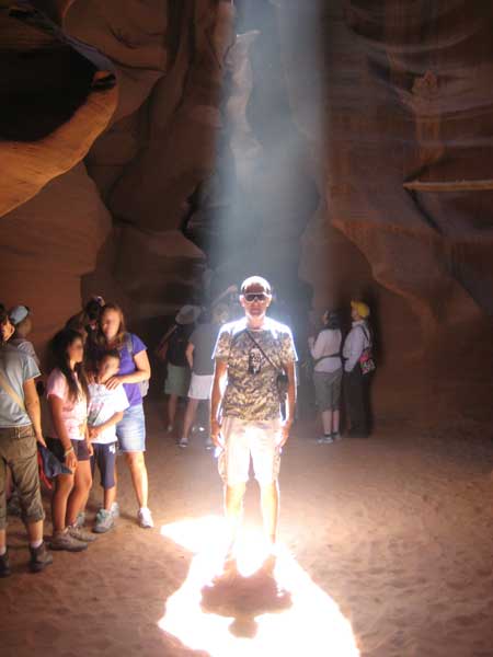 Faisceau de lumière verticale dans Upper Antelope Canyon illuminant le sol sablonneux et les visiteurs au cœur du canyon