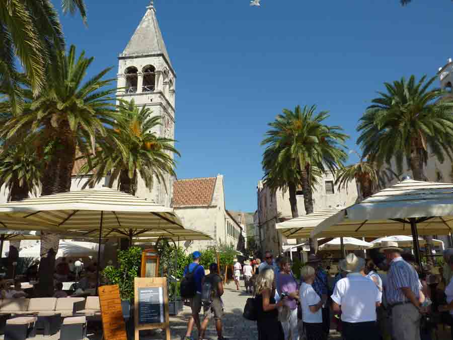 Place animée de Trogir en Croatie avec clocher de la cathédrale et palmiers, destination estivale en Dalmatie