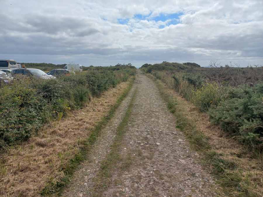 Chemin d’accès caillouteux menant aux sentiers côtiers du cap de la chèvre avec parking à proximité
