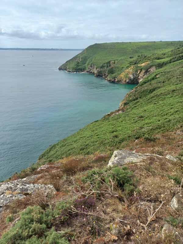 Falaises verdoyantes plongeant dans la mer au cap de la chèvre avec vue sur une crique et l’eau turquoise