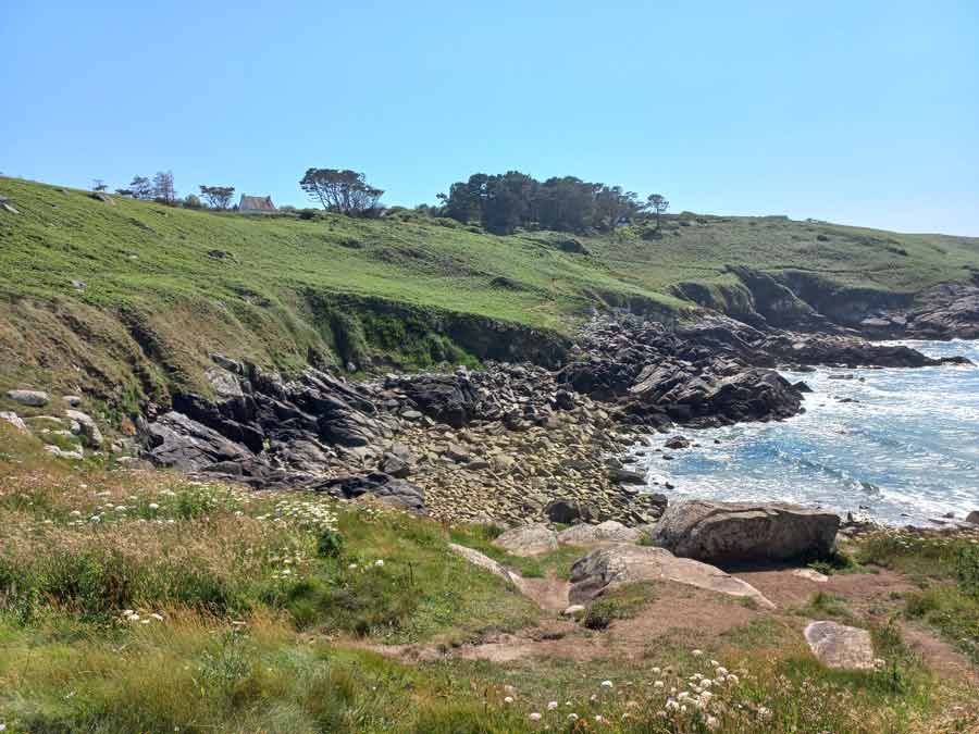 Sentier côtier longeant une crique rocheuse et les falaises verdoyantes du Cap Sizun dans le Finistère