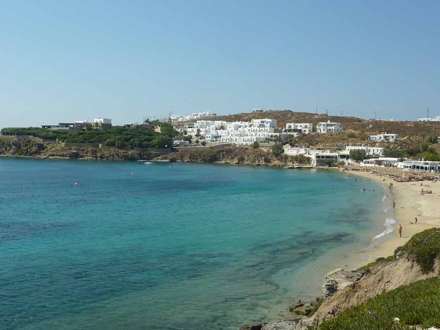 Vue panoramique de la baie d'Agios Stefanos à Mykonos, avec ses eaux bleu turquoise et ses constructions blanches en arrière-plan