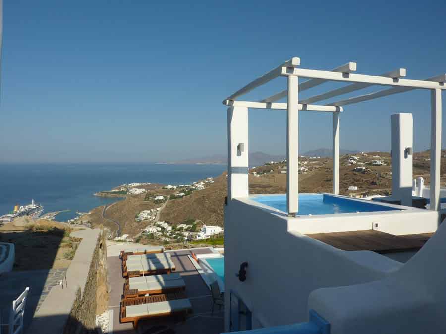 Terrasse privée avec jacuzzi et pergola blanche du Manolia View à Mykonos, offrant une vue vertigineuse sur la mer Égée, le nouveau port et les collines de l'île
