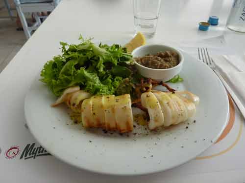 Assiette de calamars grillés accompagnés d'une salade verte et d'une sauce tapenade, servie au restaurant Avli tou Thodori à Mykonos