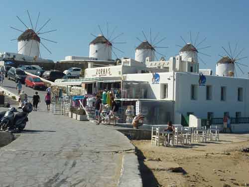 Les célèbres moulins à vent blancs de Mykonos sur leur promontoire, vus depuis la promenade animée de Chora avec ses tavernes en contrebas