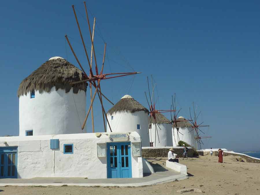La rangée de moulins à vent emblématiques de Mykonos avec leurs toits de chaume et leurs volets bleus, se découpant sur un ciel bleu immaculé au-dessus de la mer Égée