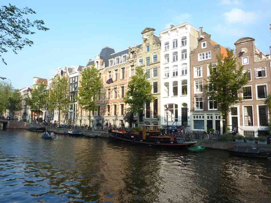 Façades colorées de maisons typiques à découvrir le long d’un canal d’Amsterdam baignées de lumière