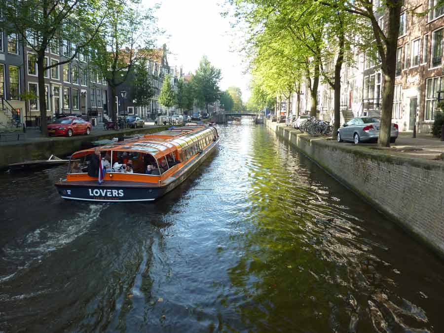 Bateau de croisière sur les canaux d’Amsterdam bordés d’arbres et de maisons typiques, activité incontournable pour découvrir Amsterdam