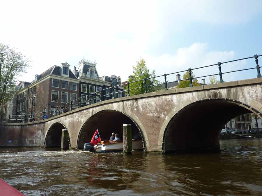 Pont en briques au-dessus d’un canal d’Amsterdam avec petite barque passant sous les arches