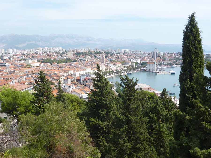 Panorama sur Split et son port depuis la colline de Marjan avec pins et cyprès au premier plan et montagnes dalmates en fond