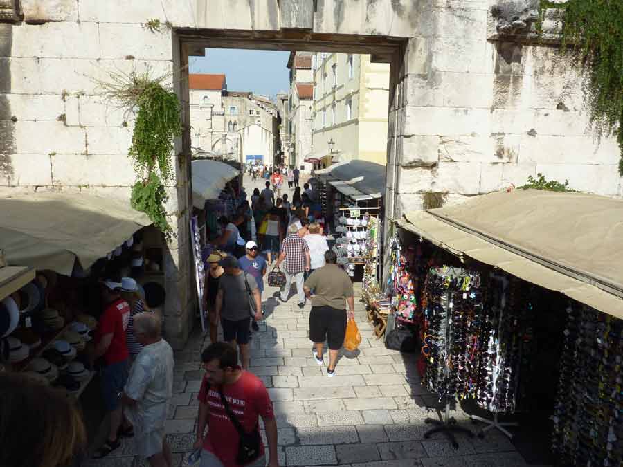Passage animé à travers une porte du palais de Dioclétien à voir Split, avec étals de souvenirs et touristes en pleine journée