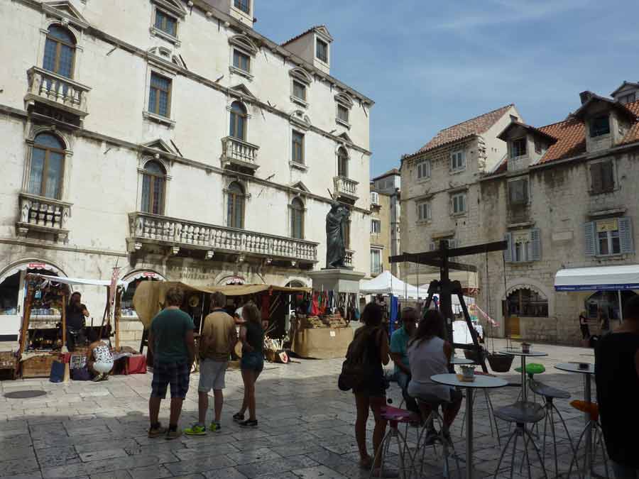 Place animée de la vieille ville de Split avec marché artisanal et façades baroques en pierre blanche

