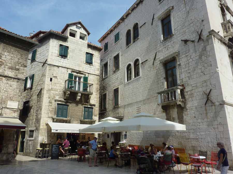 Terrasse de café ensoleillée dans une placette de la vieille ville de Split entourée de maisons en pierre dalmate