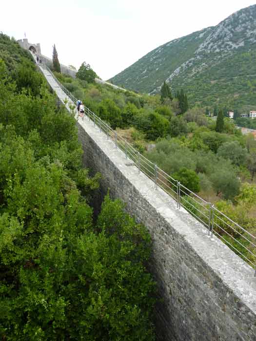 Chemin sur les remparts de Ston en Croatie avec promeneurs et vue sur la colline verdoyante