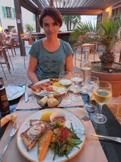 Repas en terrasse à Erbalunga avec assiette de poisson grillé et verre de vin blanc, Cap Corse