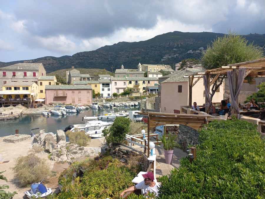 Vue sur le port de Centuri et ses maisons colorées en schiste, avec les bateaux amarrés et la montagne en arrière-plan, Cap Corse