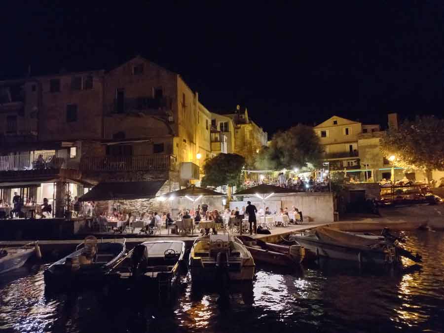 Port d'Erbalunga de nuit avec terrasses de restaurants animées et barques amarrées, Cap Corse