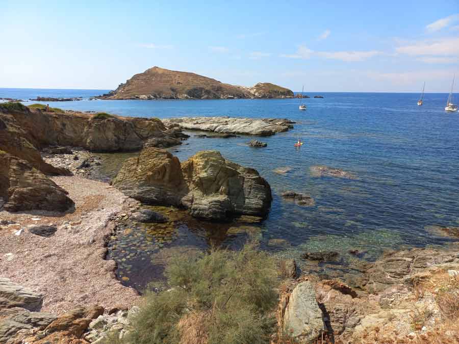 Côte rocheuse de Centuri avec rochers de schiste, eaux transparentes et îlot en arrière-plan, Cap Corse