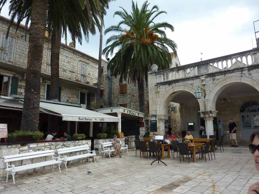 La loggia vénitienne et ses arcades de pierre sur la place Saint-Étienne de Hvar, avec terrasses de café ombragées par les palmiers