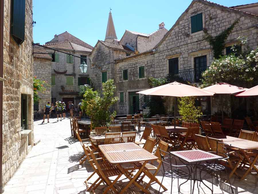 Terrasse de restaurant en plein air sur une placette de Stari Grad entourée de façades en pierre dorée, Hvar