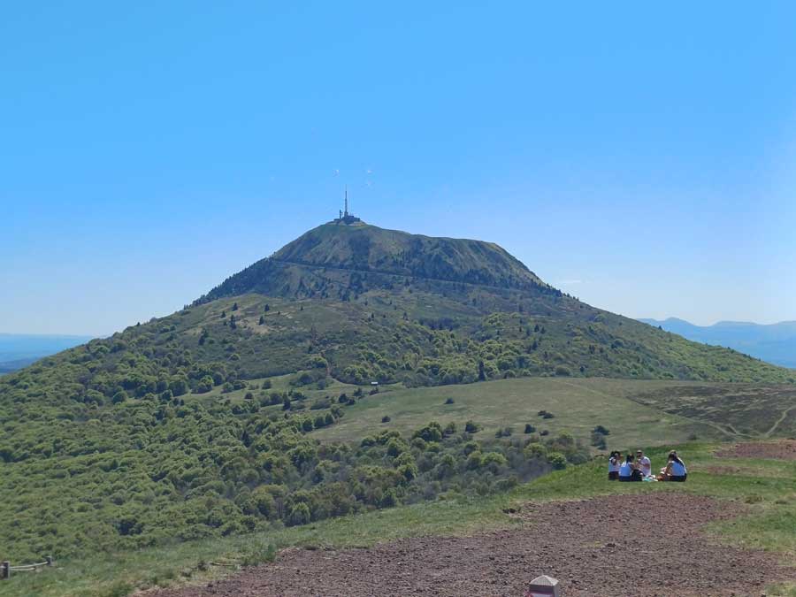 Vue imprenable sur le puy de Dôme et ses antennes depuis le sommet du puy Pariou, avec un groupe de randonneurs profitant d'un pique-nique au premier plan, panorama exceptionnel de la Chaîne des Puys classée à l'UNESCO en Auvergne