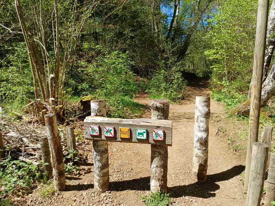 Entrée du sentier de randonnée du puy Pariou avec panneau de signalisation en bois et pictogrammes au départ du parking des Goules en Auvergne