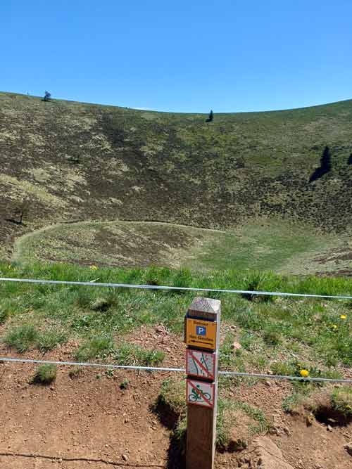Panneau d'interdiction de descendre dans le cratère du puy Pariou avec la cuvette volcanique et ses parois de scories en arrière-plan