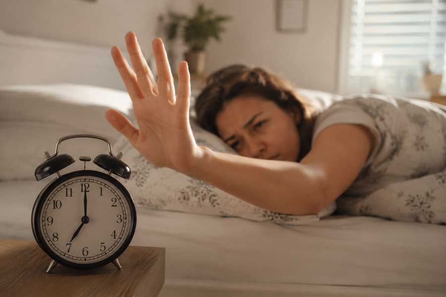 Femme fatiguée au réveil tentant d'éteindre son réveil après une nuit de sommeil écourtée lors du passage à l'heure d'été