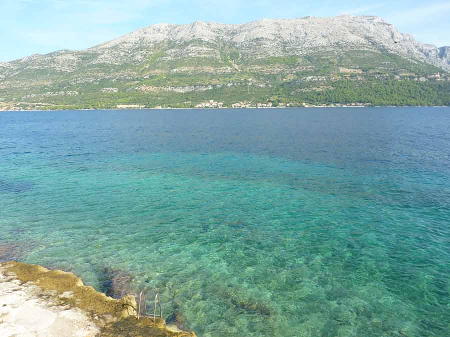 Eaux turquoise et cristallines de la plage Zakerjan à Korčula, avec vue sur les montagnes de la presqu'île de Pelješac en arrière-plan