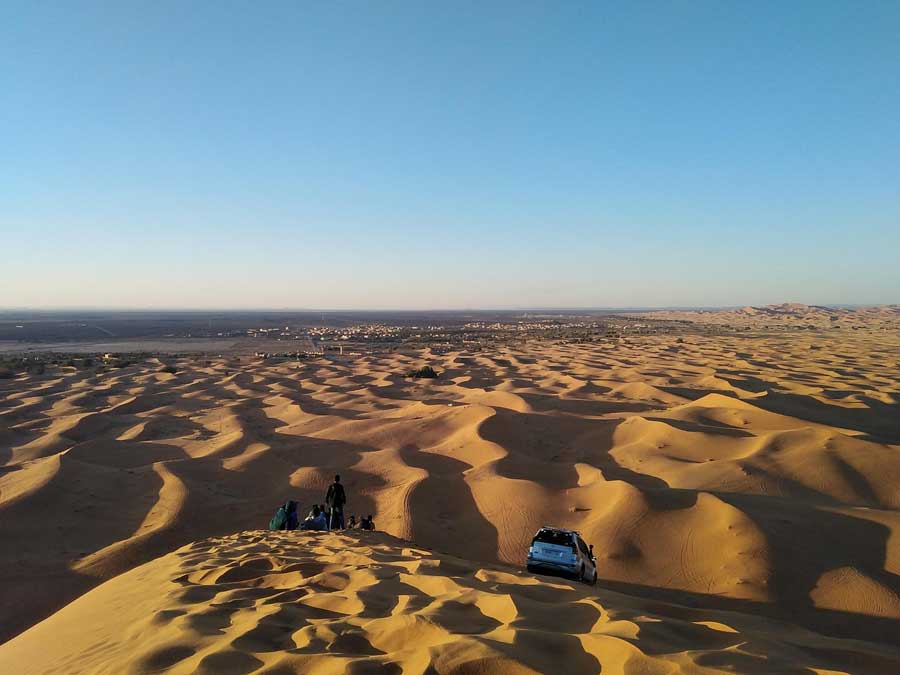 road-trip-maroc-3 Voyageurs et 4×4 au sommet d’une dune de l’Erg Chebbi en fin de journée, avec Merzouga au loin
