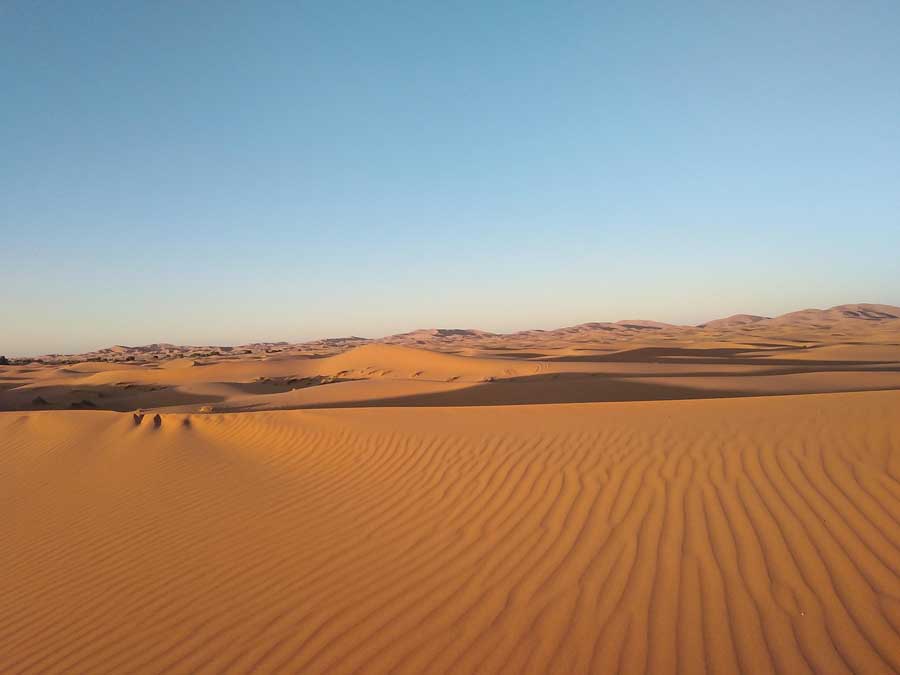 road-trip-maroc-5 Sable ridé par le vent et dunes orangées du Sahara sous un ciel sans nuage